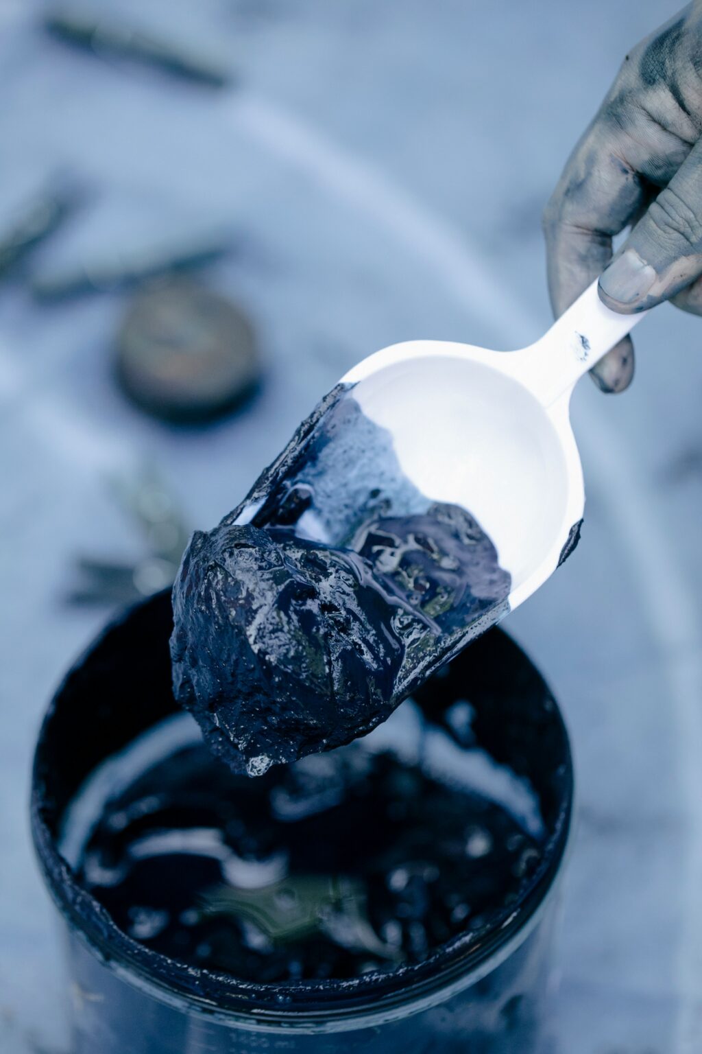 A detailed view of a hand with a spatula scooping dark mud from a jar, highlighting texture.